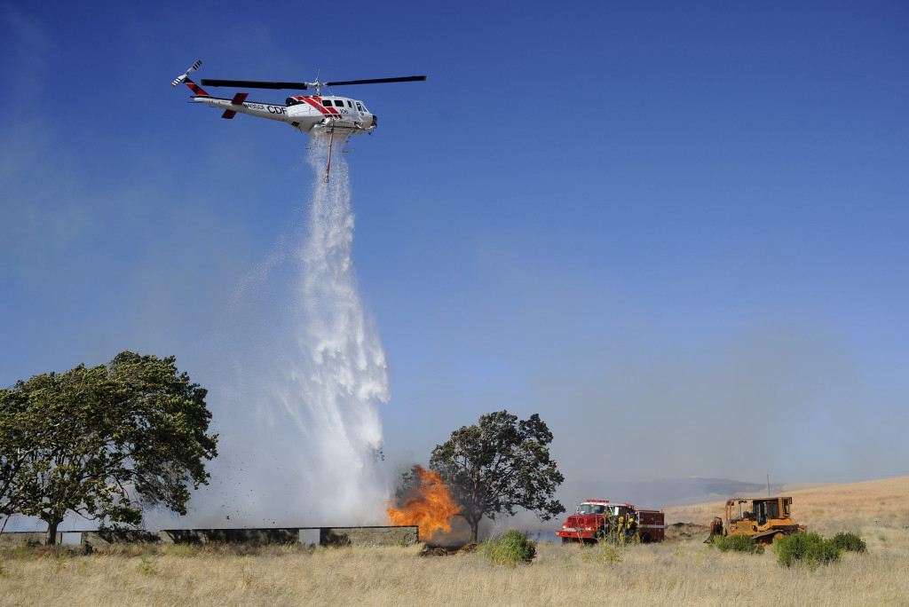 helicopter dumps water on a grass fire